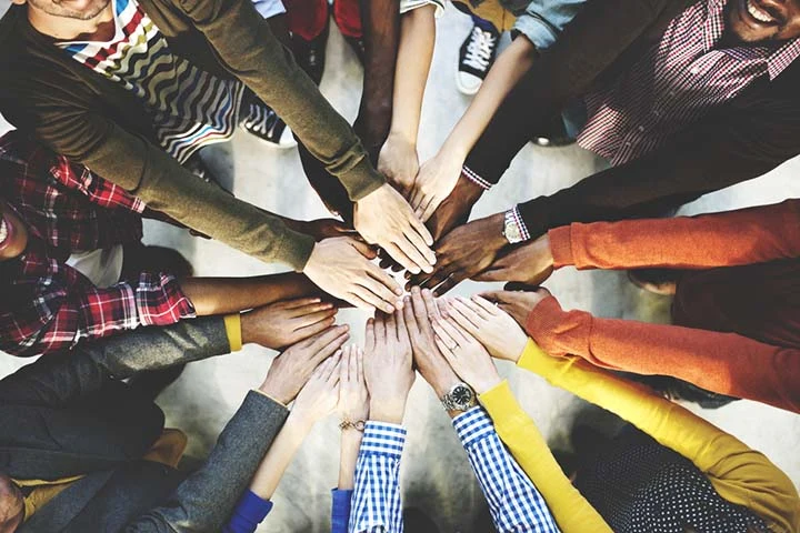 A group of people brings their hands together in the centre of a table.